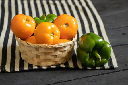 yellow tomatoes and selenium bell peppers lie on a plate on a black wooden table in the kitchen, ripe yellow tomatoes and peppersの写真素材