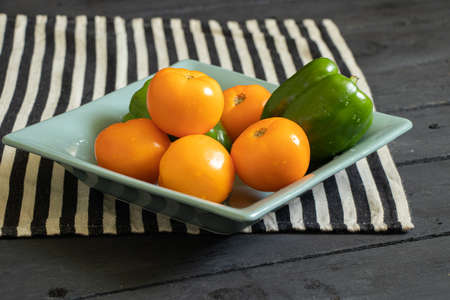yellow tomatoes and selenium bell peppers lie on a plate on a black wooden table in the kitchen, ripe yellow tomatoes and peppersの写真素材