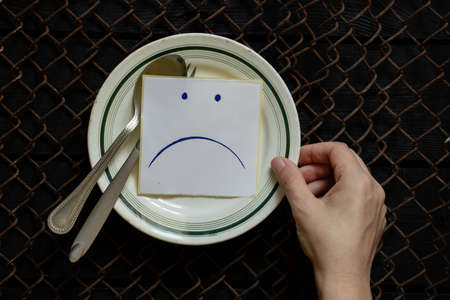 a plate of paper on which a sad smiley face and female hands are drawn, hunger and nothing to eat, a bad mood at lunchの写真素材