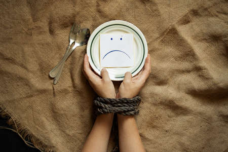 a plate with paper on which is drawn a sad smiley and women's hands tied with a rope, hunger and nothing to eat, slaveryの写真素材