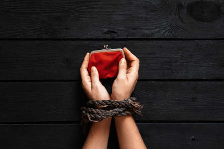 a girl with tied hands holds a red wallet on a black wooden table, a wallet in her tied handsの写真素材