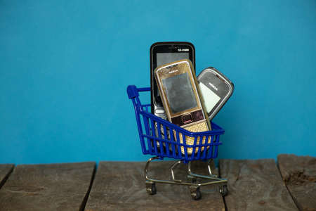 Ukraine Dnipro 08/10/2021 - phones of different models and different generations and brands are in a shopping cart for groceries on an old wooden board, many different phonesのeditorial素材
