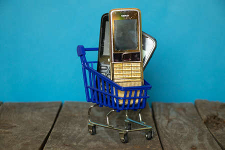 Ukraine Dnipro 08/10/2021 - phones of different models and different generations and brands are in a shopping cart for groceries on an old wooden board, many different phonesのeditorial素材