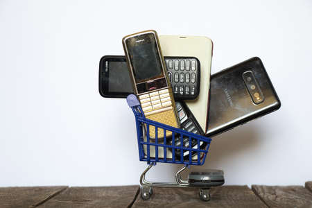 Ukraine Dnipro 08/10/2021 - phones of different models and different generations and brands are in a shopping cart for groceries on an old wooden board, many different phonesのeditorial素材