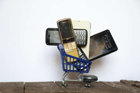 Ukraine Dnipro 08/10/2021 - phones of different models and different generations and brands are in a shopping cart for groceries on an old wooden board, many different phonesのeditorial素材