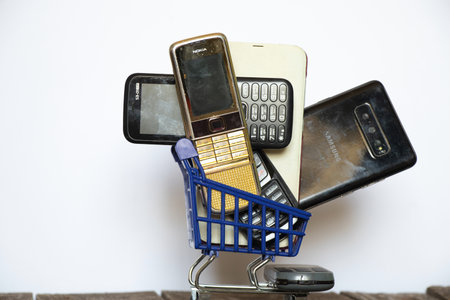 Ukraine Dnipro 08/10/2021 - phones of different models and different generations and brands are in a shopping cart for groceries on an old wooden board, many different phonesのeditorial素材