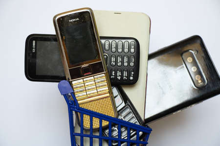 Ukraine Dnipro 08/10/2021 - phones of different models and different generations and brands are in a shopping cart for groceries on an old wooden board, many different phonesのeditorial素材