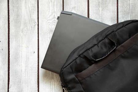black laptop and black laptop bag lie on the written old wooden table, laptop on the table