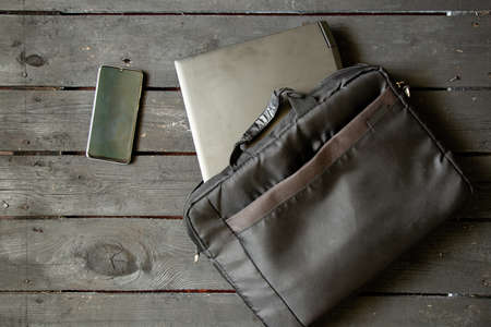 black laptop and black laptop bag and phone lie on the written old wooden table, laptop on the table and phoneの写真素材