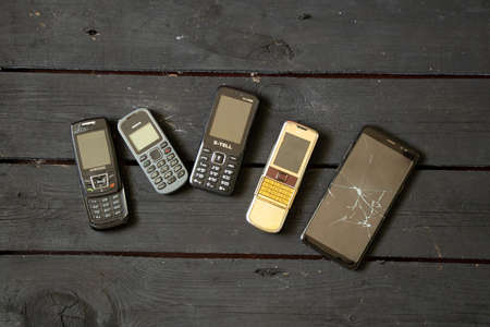 Ukraine Dnipro 08/10/2021 - phones of different models and different generations and brands lie on an old wooden board, many different phonesのeditorial素材