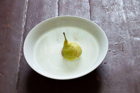 a pear in water in a white mask stands on a table by the window, wash a pear in a plateの写真素材