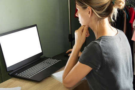 a girl sits at a table and looks at a laptop with a poor screen at home, working on self-isolation at home, a laptop with a poor screenの写真素材
