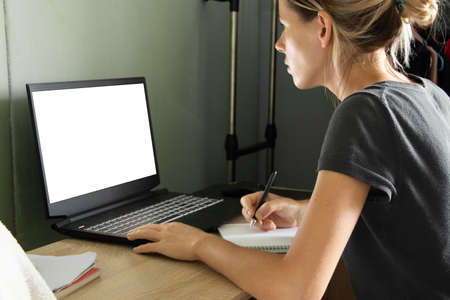 a girl sits at a table and looks at a laptop with a poor screen at home, working on self-isolation at home, a laptop with a poor screenの写真素材