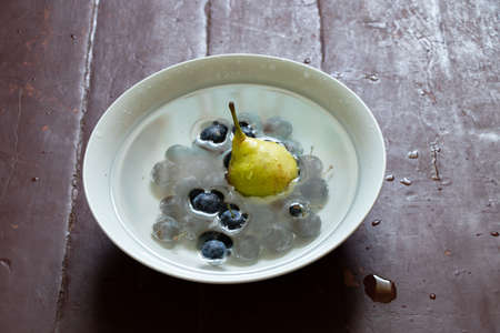 pear and plums in water in a white mask stands on the table by the window, wash the pear in a plateの写真素材
