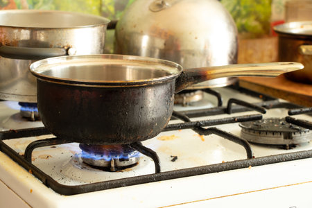 a dirty saucepan stands on a dirty gas stove in the kitchen at home, cooking soup on the stove, gas...