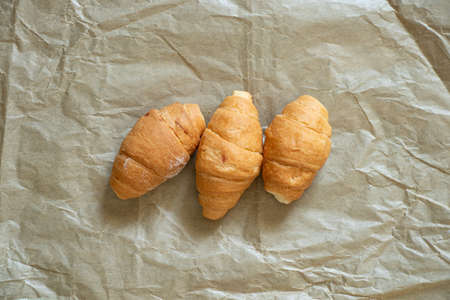 three croissants lie on crumpled brown paper in a cafe, croissants