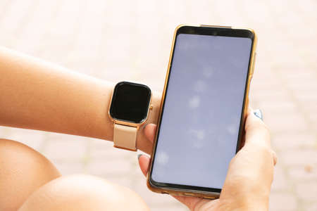 smart watch and a phone with a white screen in the hands of a girl in the park, new technologies and people, a watch and a phoneの写真素材