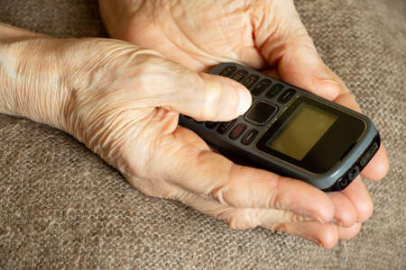 old woman's hands hold push-button telephone at home, pensioner with telephoneの写真素材