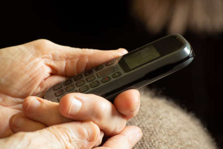 old woman's hands hold push-button telephone at home, pensioner with telephoneの写真素材