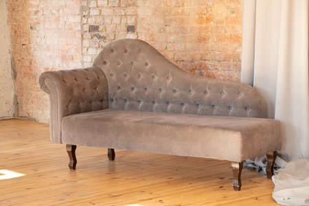 gray upholstered armchair carried a brick brown wall in an apartment on a wooden floor, upholstered...
