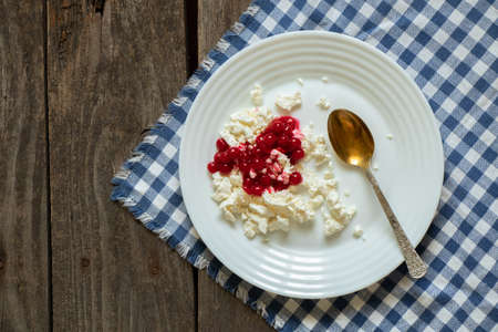 homemade cottage cheese with viburnum on a white plate is on a tablecloth on an old wooden table, cottage cheese for breakfast, cottage cheese with viburnum on a plateの写真素材