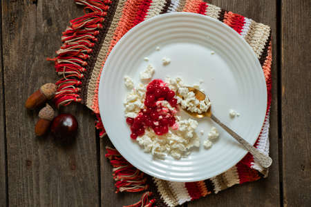 homemade cottage cheese with viburnum on a white plate is on a tablecloth on an old wooden table, cottage cheese for breakfast, cottage cheese with viburnum on a plateの写真素材