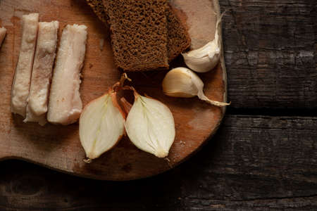 a piece of bacon onion garlic black bread on a wooden table, home-style lunch with baconの写真素材