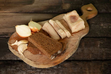 a piece of bacon onion garlic black bread on a wooden table, home-style lunch with baconの写真素材