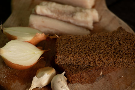 a piece of bacon onion garlic black bread on a wooden table, home-style lunch with baconの写真素材