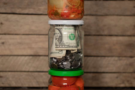 dollars and pennies closed in a glass jar stand next to canned vegetables at home on a shelf, saving...
