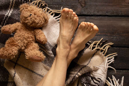 female legs on a brown plaid blanket lying next to a teddy bear on a wooden floor, legs on a wooden floor, home comfort and relaxation, legsの写真素材