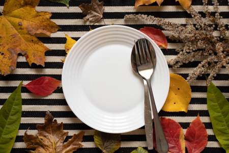 Dinner plate stands on a striped black and white background in autumn yellow-red leaves, autumn...