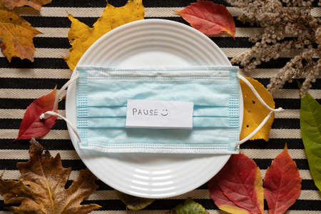 the word pause on paper lies on a medical mask in a plate on a striped background in autumn leaves,...