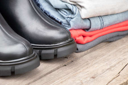 women's high black boots with thick soles and a pile of things stand on a wooden board in the sun on the street, women's shoes and winter clothes, fashionable clothes and shoes, thingsの写真素材