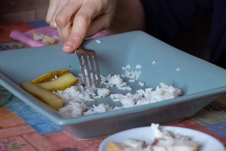 old woman at the dining table on the table rice cucumbers and lard, woman's hands at the table in the kitchen for lunch, food on the table beforeの写真素材