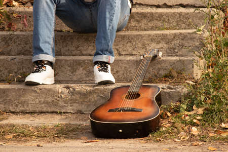 old brown guitar lies in the park on the steps near a man in the autumn in the sun, guitar, hobbyの写真素材