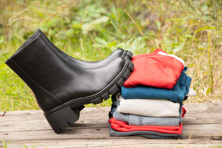 women's high black boots with thick soles and a pile of things stand on a wooden board in the sun on the street, women's shoes and winter clothes, fashionable clothes and shoes, thingsの写真素材