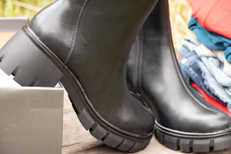 women's high black boots with thick soles and a pile of things stand on a wooden board in the sun on the street, women's shoes and winter clothes, fashionable clothes and shoes, thingsの写真素材