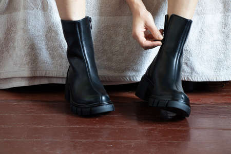 girl in high black boots on the old dirty floor at home, women's shoes, feet in shoes on the floor, shoes on the wooden floorの写真素材