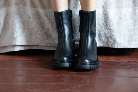 girl in high black boots on the old dirty floor at home, women's shoes, feet in shoes on the floor, shoes on the wooden floorの写真素材