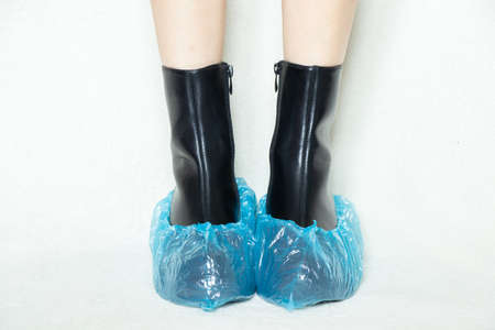 girl in high black boots on a white background in disposable medical boots, women's shoes, feet in shoes on the floor, women's legs in boots on a white background in a hospital in bohilasの写真素材