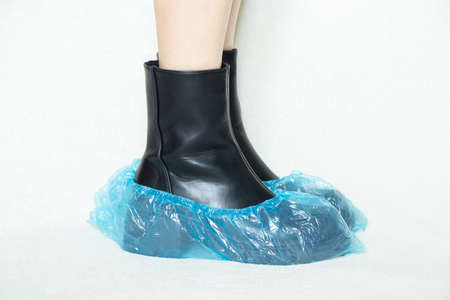 girl in high black boots on a white background in disposable medical boots, women's shoes, feet in shoes on the floor, women's legs in boots on a white background in a hospital in bohilasの写真素材