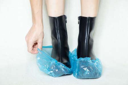 girl in high black boots on a white background in disposable medical boots, women's shoes, feet in shoes on the floor, women's legs in boots on a white background in a hospital in bohilasの写真素材