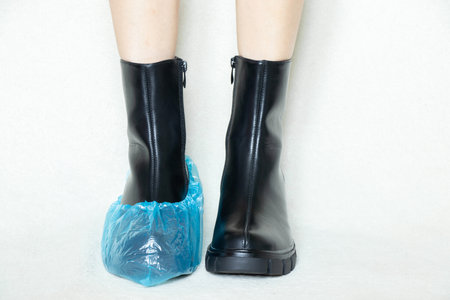 girl in high black boots on a white background in disposable medical boots, women's shoes, feet in shoes on the floor, women's legs in boots on a white background in a hospital in bohilasの写真素材
