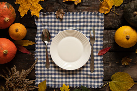 white plate on the tablecloth stands on a wooden table next to pumpkins and autumn leaves, festive...