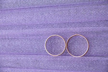 two gold wedding rings of the bride and groom lie on purple fabric, wedding ringsの写真素材