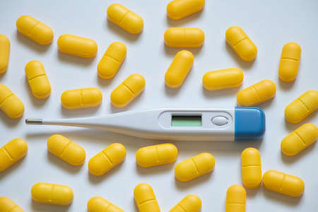 electronic thermometer lies next to yellow pills on an isolated background, medicine and pharmacy,...