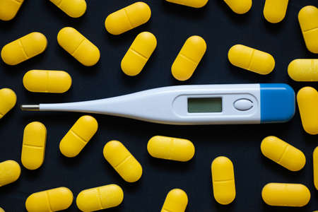 electronic thermometer lies next to yellow pills on an isolated background, medicine and pharmacy, health and treatment, pills and antibioticsの写真素材