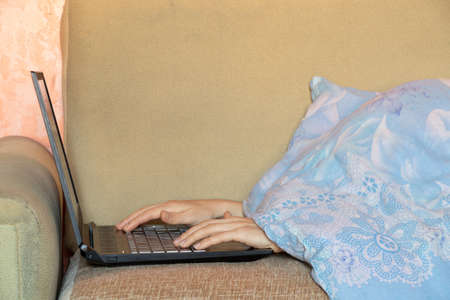 female hands on the laptop keyboard on the bed in a blanket, working at home in a laptop on the bed...