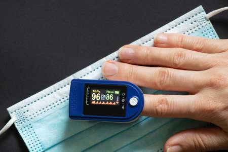 woman's finger pulse oximeter and disposable medical mask on isolated background, measure blood...